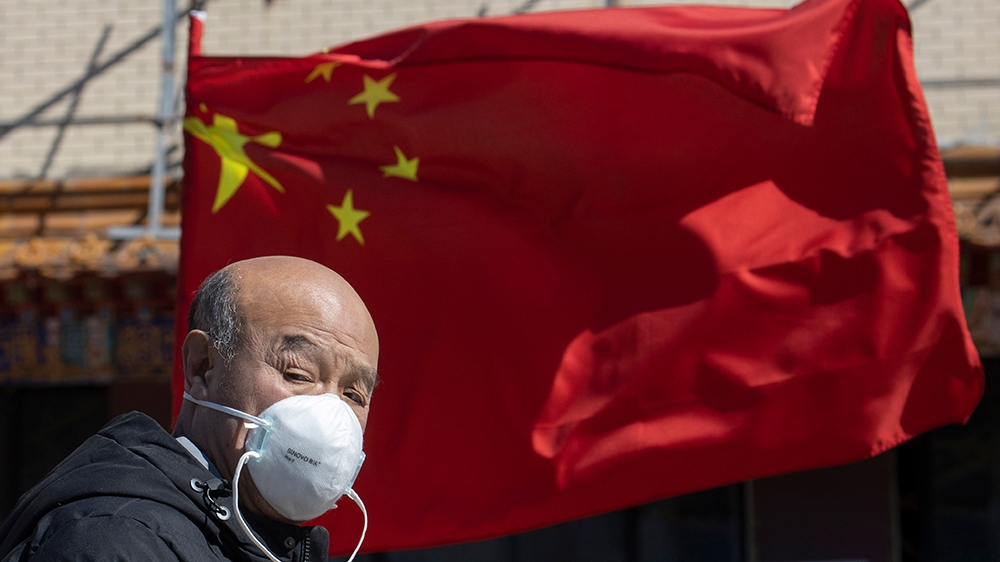 A masked man walks past a national flag outside a traditional medicine hospital in Beijing on Tuesday, March 3, 2020. Mushrooming outbreaks in the Mideast, Europe and South Korea contrasted with optim