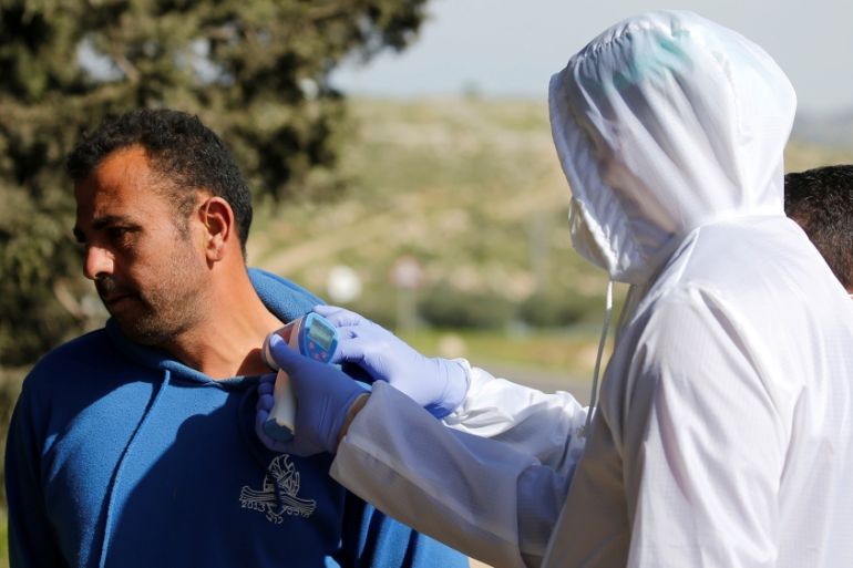 A member of medical staff checks the body temperature of a Palestinian worker returning from Israel, amid concerns over the spread of the coronavirus disease (COVID-19), outside the Israeli-controlled