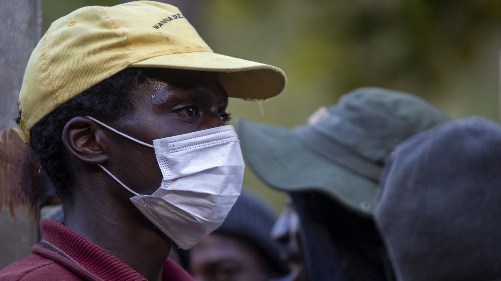 A man wearing face masks to protect herself against coronavirus, mends the gate as homeless people are queuing for a meal and a shelter in Hillbrow, Johannesburg, South Africa, Friday, March 27, 2020.