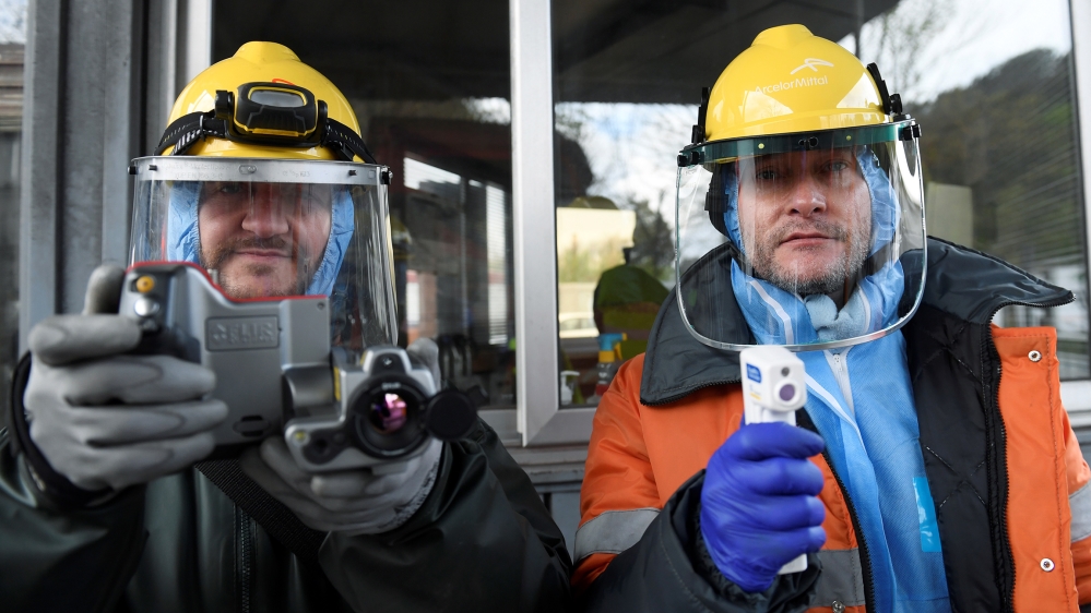 Workers from the multinational ArcelorMittal pose with a thermal camera and a digital thermometer with which they use to take the temperature of personnel entering a factory, to help combat the spread