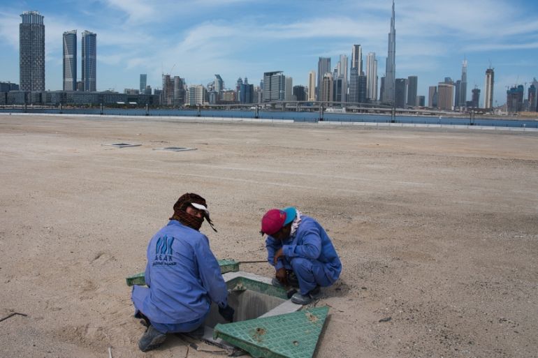 Two construction workers examine a drainage system with the Burj Khalifa, the world''s tallest building, in the skyline behind them in Dubai, United Arab Emirates, Monday, April 6, 2020. Dubai, one of