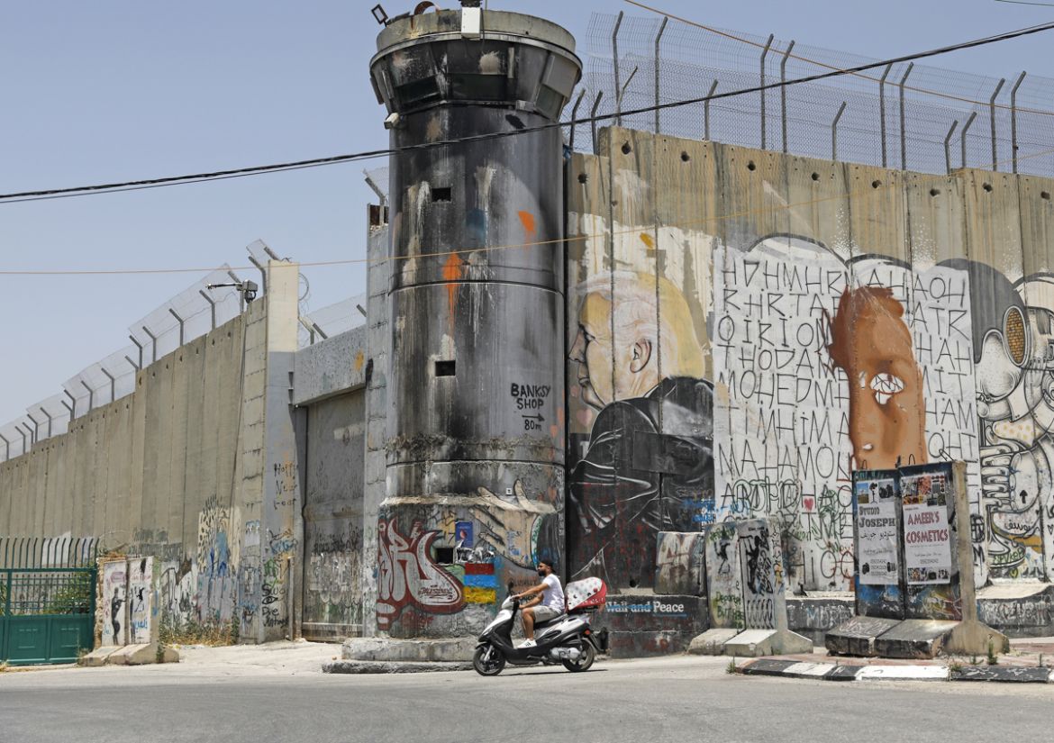 A Palestinian man rides his motorcycle past a mural painting of US President Donald Trump on Israel''s controversial separation barrier in the West Bank city of Bethlehem on June 8, 2020. (Photo by AHM