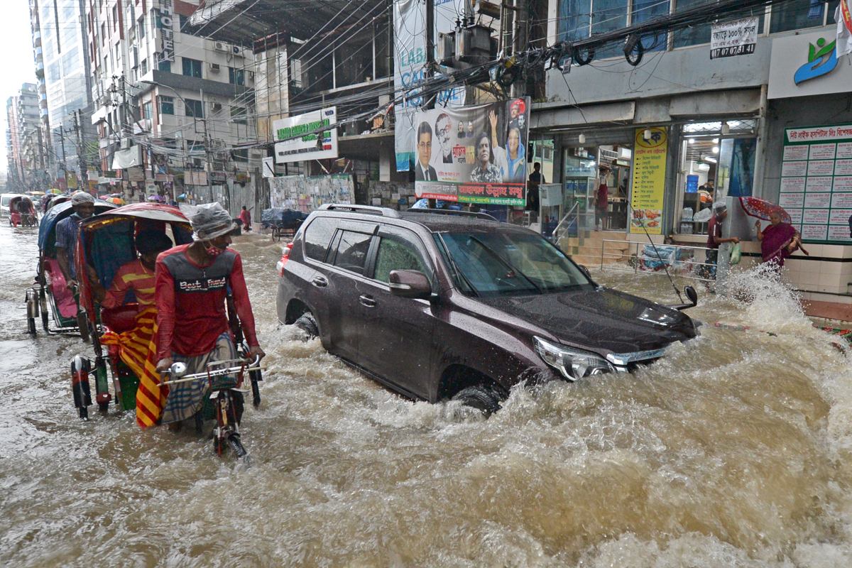 Commuters make their way through a water-logged street after a heavy downpour in Dhaka on July 21, 2020. - The death toll from heavy monsoon rains across South Asia has climbed to nearly 200, official