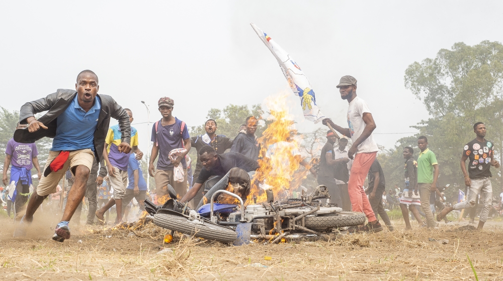 Demonstrators stand next to a burning motorcycle during a protest where demonstrators and police officers clashed in Kinshasa on July 9, 2020 in demonstrations organized against the presidential party