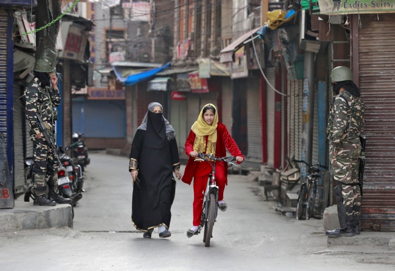 A Kashmir girl rides her bike past Indian security force personnel standing guard in front closed shops in a street in Srinagar, October 30, 2019. REUTERS/Danish Ismail TPX IMAGES OF THE DAY