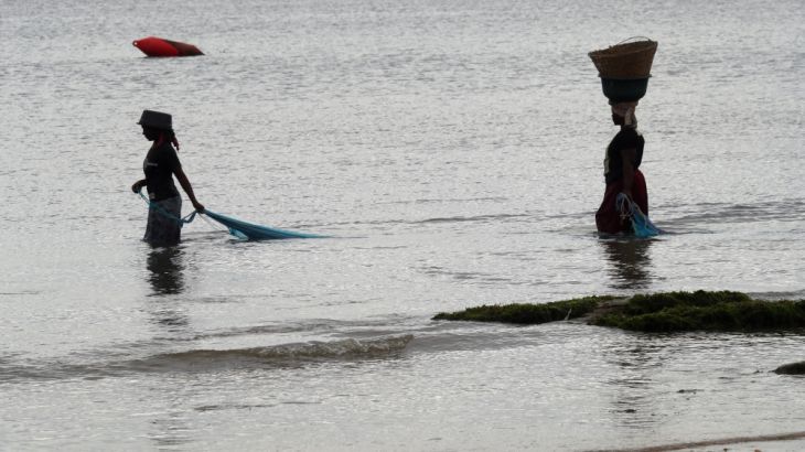 Women carry nets along a beach in Pemba
