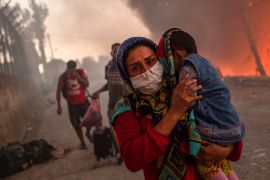 A woman carries a child past flames after a major fire broke out in the Moria migrants camp on the Greek Aegean island of Lesbos, on September 9, 2020. - Thousands of asylum seekers were left homeless