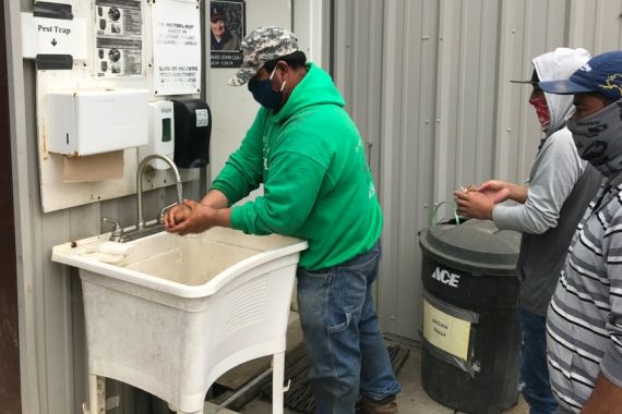 Farmworkers wash their hands before returning to work at a farm outside of Half Moon Bay, California [Brian Osgood/Al Jazeera]