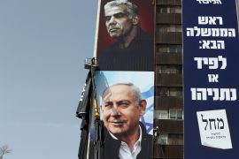 Labourers hang a Likud party election campaign banner depicting party leader Israeli Prime Minister Benjamin Netanyahu and his challenger Yesh Atid party leader Yair Lapid, ahead of a March 23 ballot, in Jerusalem March 10, 2021. The writing in Hebrew reads: &#39;Next Prime Minister: Lapid or Netanyahu&#34;. [Ammar Awad/Reuters]