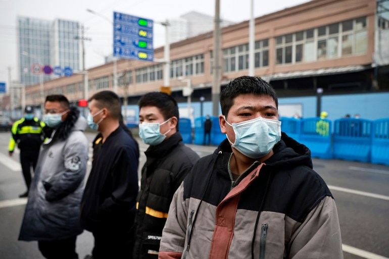 Plainclothes security officials guarding the Huanan market, cordoned off behind blue plastic bollards, during the visit of the WHO expert team to Wuhan in January 2021
