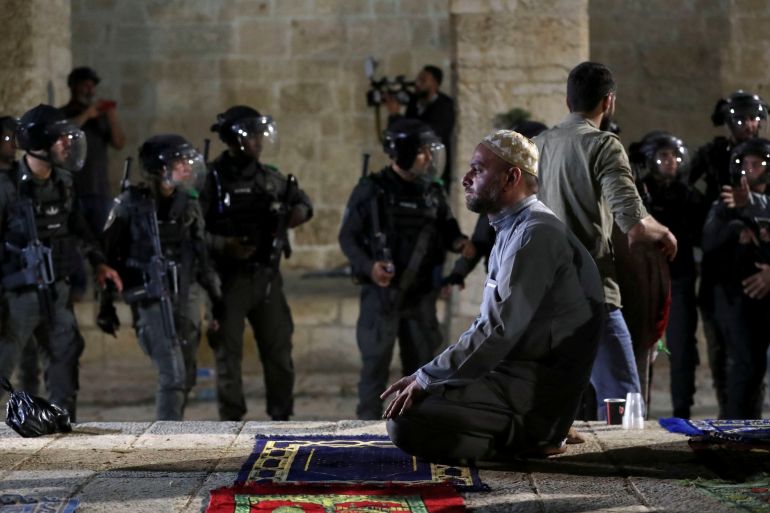 A Palestinian man prays as Israeli police gather.