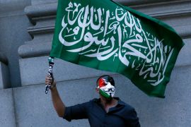 A man wearing a mask holds a Hamas flag.