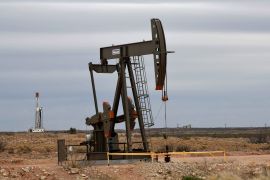 A pump jack operates in front of a drilling rig owned by Exxon near Carlsbad, New Mexico