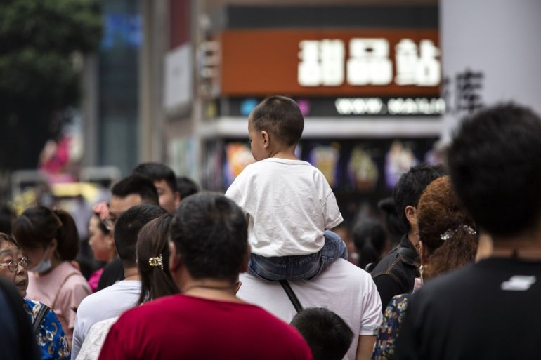 A child is carried on a man's shoulders in the middle of a crowded city sidewalk.