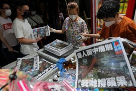 A woman hands out final editions of the Apple Daily as people queue to buy it.