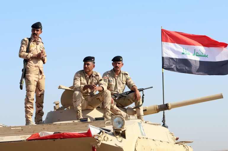 Iraqi army officers sit on a military vehicle.