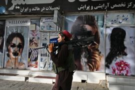 A Taliban fighter walks past a beauty salon with images of women defaced using spray paint in Shar-e-Naw in Kabul on August 18, 2021 [AFP/Wakil Kohsar]