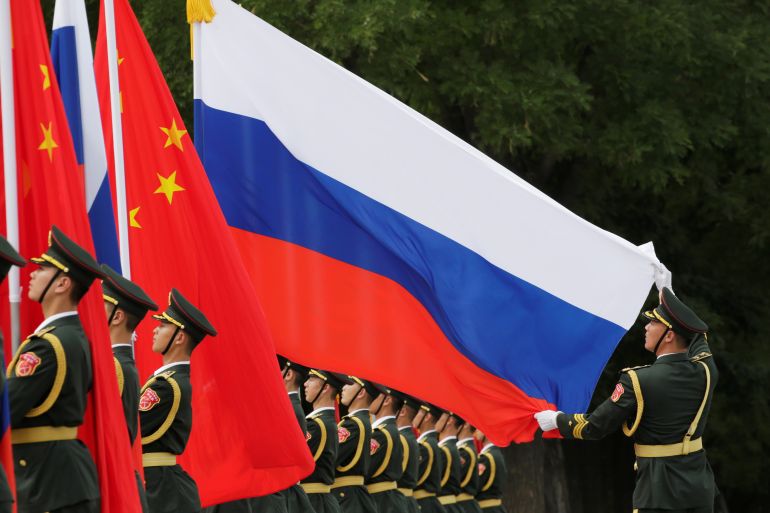 A military officer adjusts a Russian flag ahead of a welcome ceremony hosted by Chinese President Xi Jinping