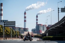 A man rides his scooter near the Shanghai Waigaoqiao Power Generator Company coal power plant [File: AFP/Johannes Eisele]