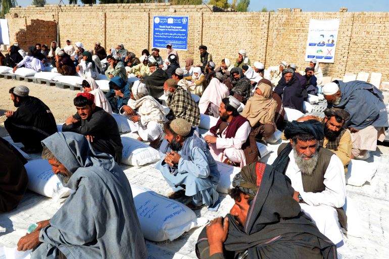 Afghan people sit besides sacks of food grains distributed as an aid by the World Food Programme (WFP) in Kandahar.
