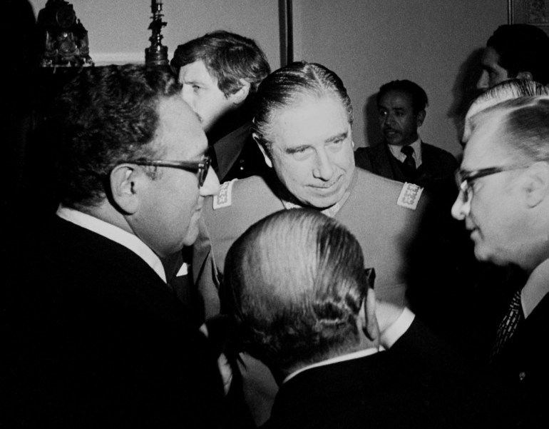 Henry Kissinger and Augusto Pinochet stand in a small circle of men.
