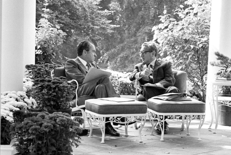Richard Nixon and Henry Kissinger in discussion on an outdoor patio.