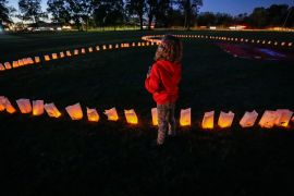 A child stands next to candles representing unmarked Indigenous child graves