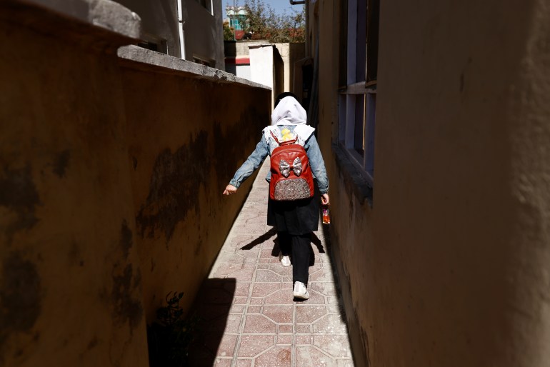 An Afghan schoolgirl walks down a street, her back to the camera