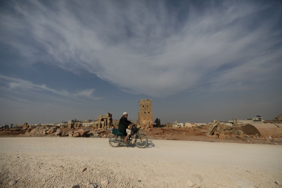 A man rides a motorcycle through the archaeological site of Sarjableh, Syria