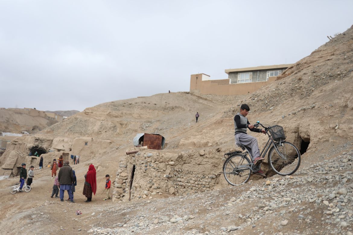 A boy rides a bicycle near houses on a hillside in Bamiyan, Afghanistan