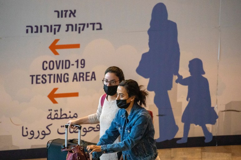 Travelers wearing protective face masks arrive at Ben Gurion Airport near Tel Aviv, Israel, Sunday, Nov. 28, 2021. Israel on Sunday approved barring entry to foreign nationals and the use of controversial technology for contact tracing as part of its efforts to clamp down on a new coronavirus variant