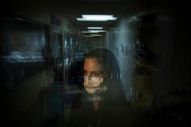 A masked woman is viewed through a pane of glass.