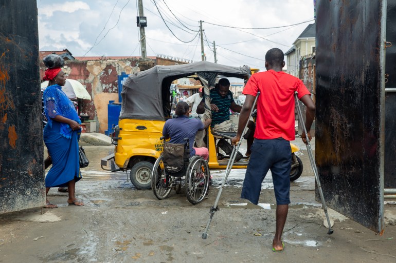 Olajumoke boards an inaccessible keke napep – a yellow and black tricycle. A man with an amputated leg using crutches and a woman watch.