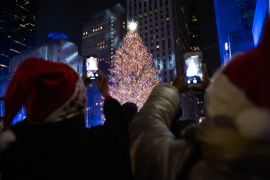 People wearing Santa Claus hats take photos of the annual Rockefeller Christmas Tree lit up during the Rockefeller Center Christmas Tree lighting ceremony on December 1, 2021, in New York City [Alexi Rosenfeld/Getty Images]