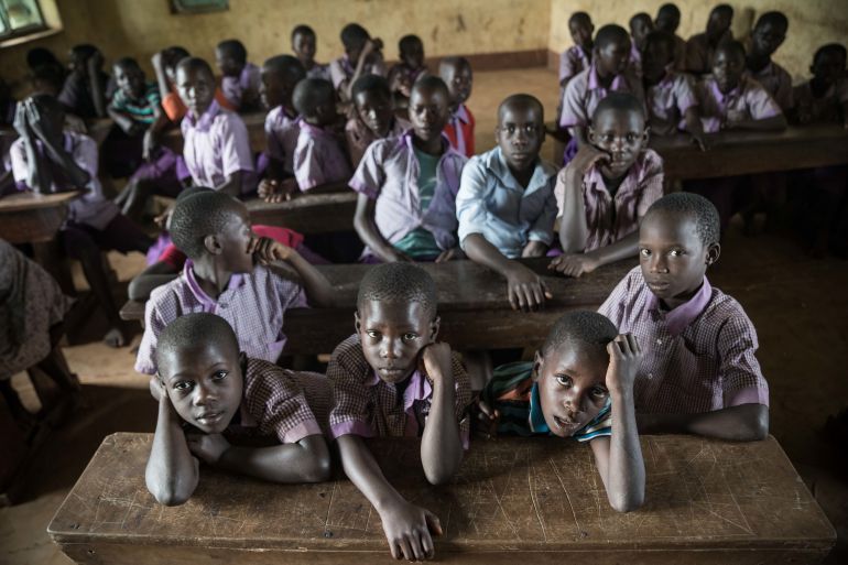 Ugandan pupils are sitt on benches inside a class.