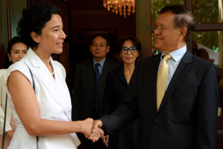 Kem Sokha in a dark suit and white shirt shakes hands with French ambassador Eva Nguyen Bin, who is wearing a white sleeveless blouse, on the porch of his home in Phnom Penh