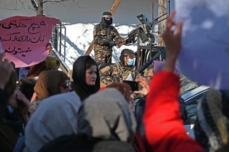 Taliban fighters stand guard as Afghan women protest.