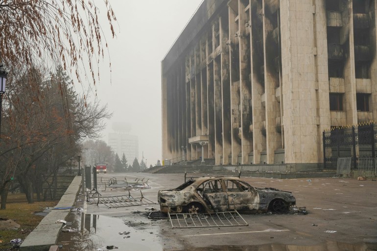 A torched vehicle lies in front of a burnt-out administrative building in central Almaty