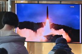 People watch a television screen showing a news broadcast with file footage of a North Korean missile test.