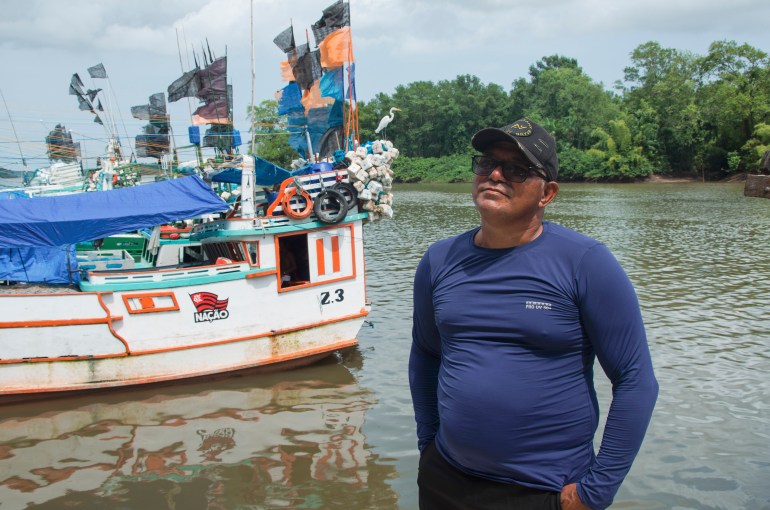 Silvio Sardinha is a boat captain standing by the water and a boat wearing sunglasses and a long-sleeved blue t-shirt