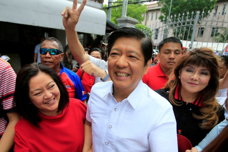 'Bongbong' Marcos in a white shirt and accompanied by his wife and sister smiles to a crowd.