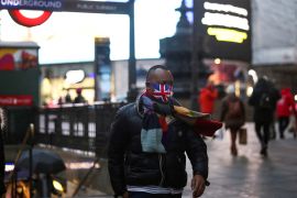 A person wearing a protective face mask walks through Piccadilly Circus, London amid the COVID outbreak