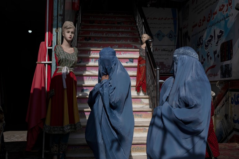 Burka-wearing Afghan women walk past a clothing shop, in Herat