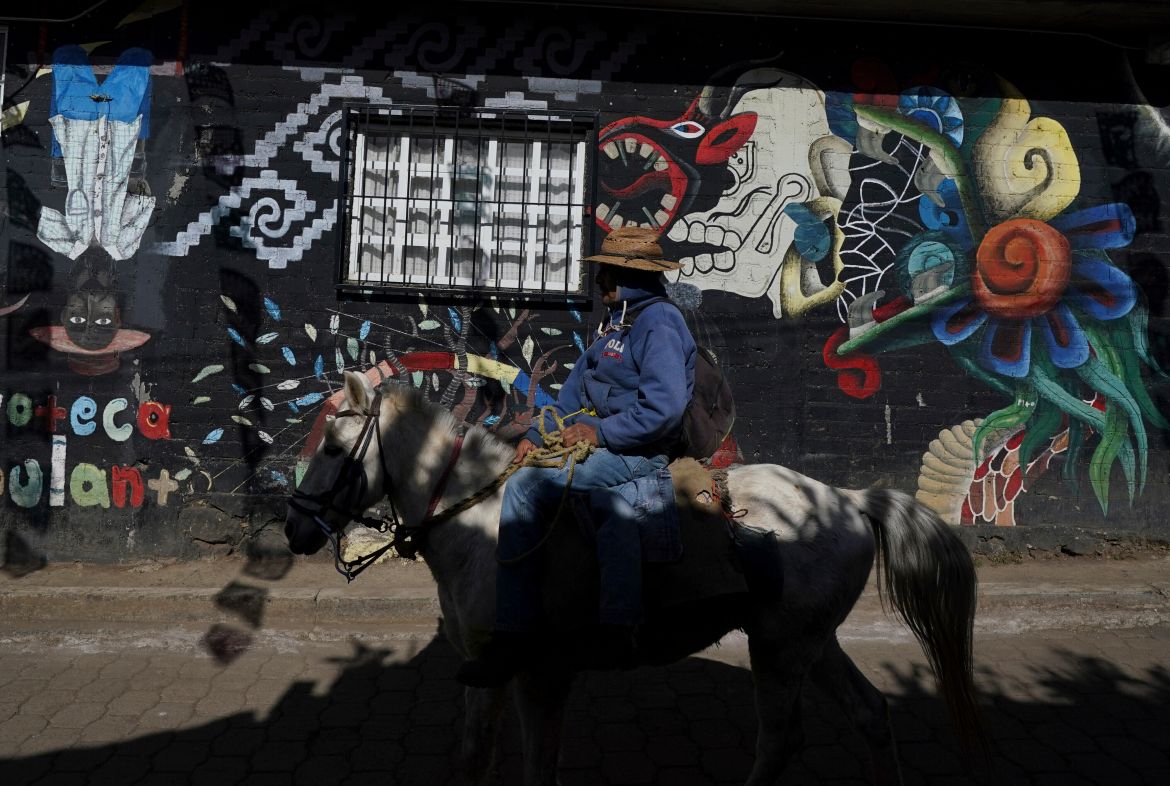 A farmer rides his horse past a mural in the Puerpecha Indigenous community of Comachuen, Mexico