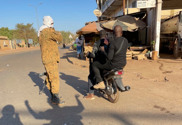 Two men ride past a military checkpoint outside a military base in Burkina Faso's capital Ouagadougou Sunday Jan. 23, 2022. Witnesses are reporting heavy gunfire at a military base raising fears that a coup attempt is underway. Governm