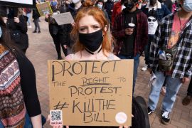 A femal protester wearing a black mask holds a sign that reads "Protect the right to protest, kill the bill"