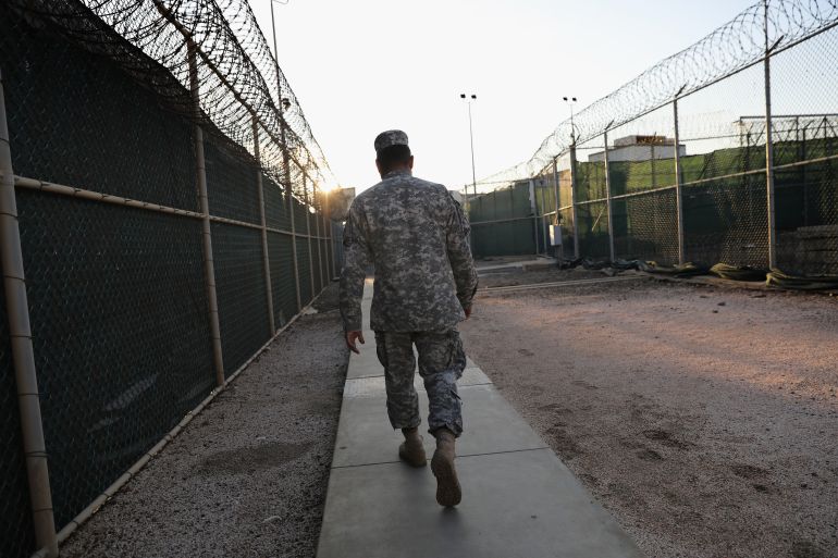 a US soldier walks between two gates with razor wires on top of both gates in Guantanamo bay.