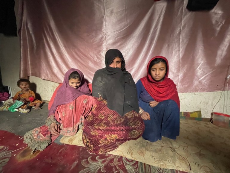 Afghan woman named Zaigul sits on the floor of her home with her children.
