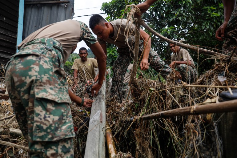 Three Malaysian soldiers in fatigues clear debris after flooding devastated the Hulu Langat area near Kuala Lumpur 