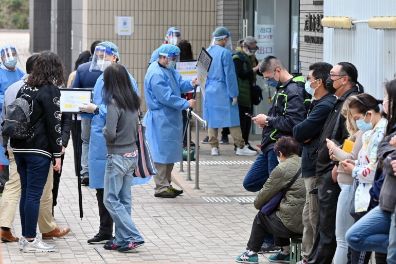 People queue in a line opposite medical workers in full protective equipment to get COVID-19 tests